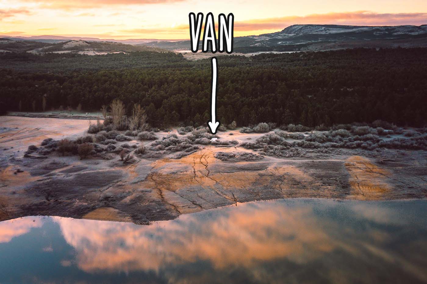 view of campervan with lake in foreground and pine forest in background