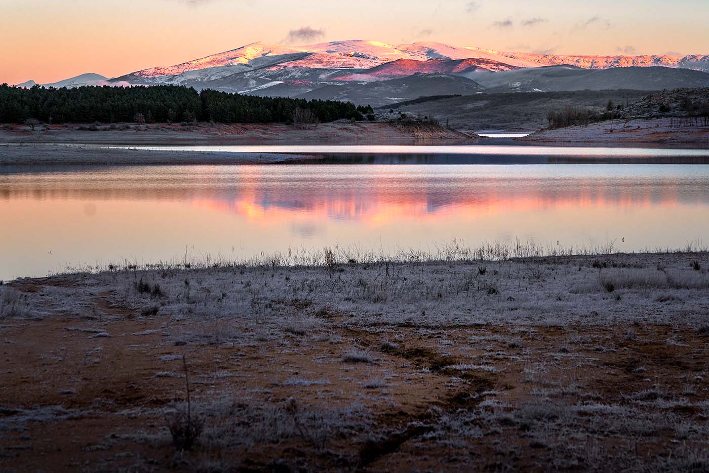 Cantabrian mountains at sunrise with pink light and still lake in foreground