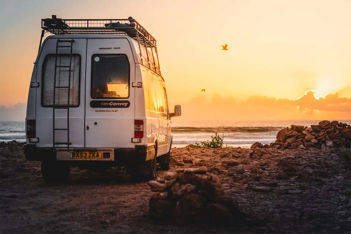 campervan on beach at sunset with birds in the sky